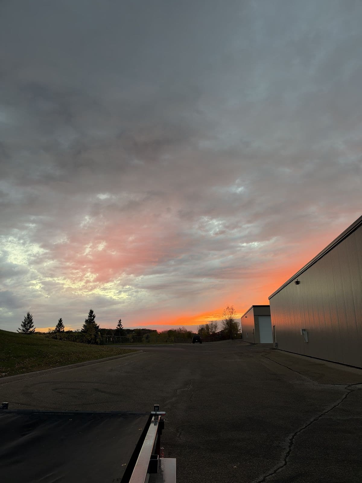 An orange sunset over a parking lot beside a metal building
