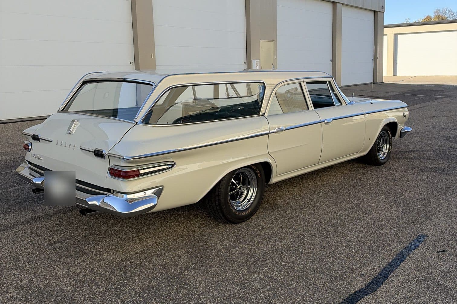 A cream station wagon with chrome trim, parked in front of a row of garage doors